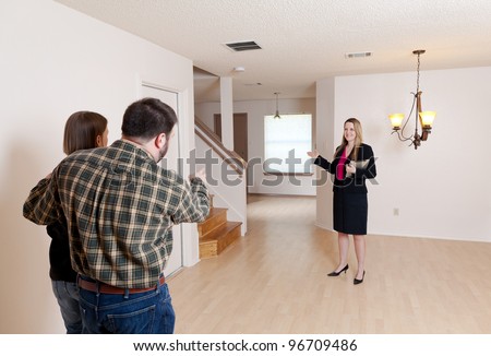 A female real estate agent shows an empty home to a husband and wife who are prospective buyers.