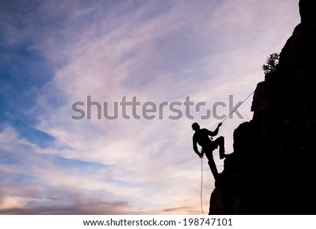 A man rappels down a mountain face during sunset