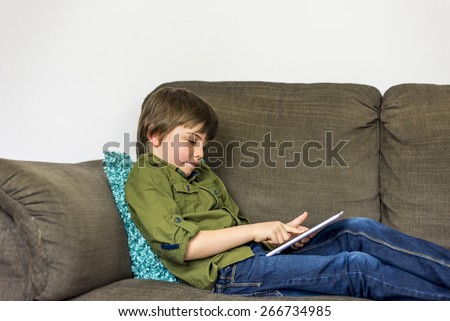 boy laying relaxed on sofa playing on his tablet