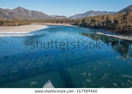 The shadow of the bridge reflected in the turquoise water in the river, on which small pieces of ice floating