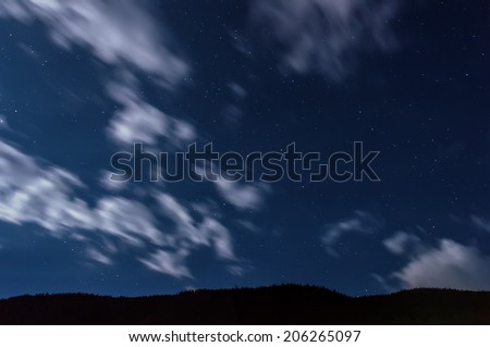 Stars and clouds on the sky, shot long exposure, on a background the dark contour of the mountains.