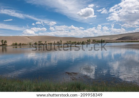 Scenic landscape with a lake in the steppe, the blue sky and clouds reflected in the water and mountains in the background