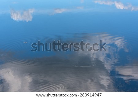 Abstract natural background of the lake water, the reflections of the sky and clouds, circles on the water and beautiful small waves