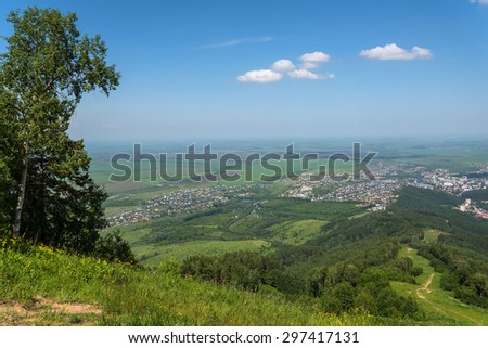 Scenic top view on the town, trees, forest, agricultural fields, farms and villages on the background of blue sky and clouds in summer
