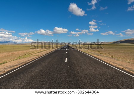 Scenic view from the asphalt road in the steppe on a background of mountains and blue sky with clouds