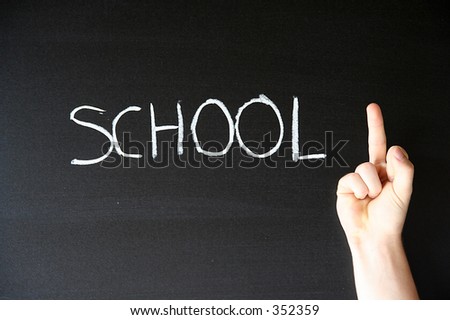 black chalkboard with word \'school\' written on it. A hand with middle finger up in front of it