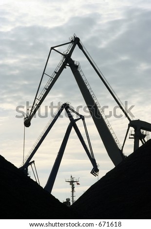 Crane silhouettes in a harbor.  Piles of coal in front