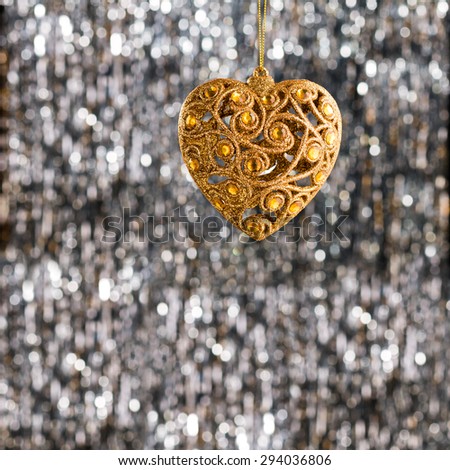 Gold heart Christmas ornament over silver glitter background