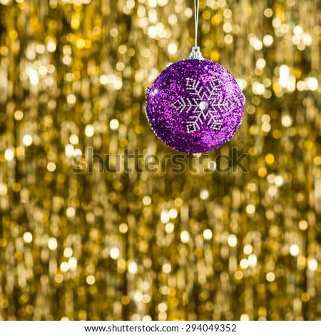 Purple Christmas tree bauble in front of gold glitter background