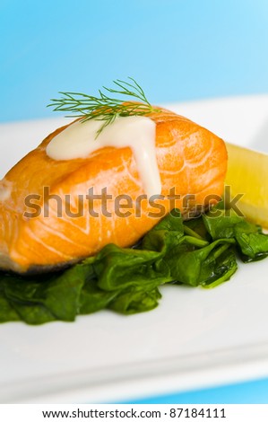 Salmon steak on spinach, decorated with lemon, sauce and dill