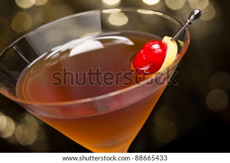 Manhattan cocktail garnished with a cherry and lemon and gold glitter back ground