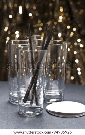 Long drink glasses with straws and coaster in front of glitter background in front of gold glitter background