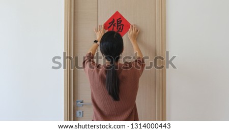 Woman stick chinese red calligraphy on the door for decorating chinese new year, word mean luck