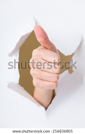 Thumb up hand gesture break through the paper wall