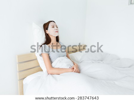 Asian woman using paper mask on face and lying down on the bed