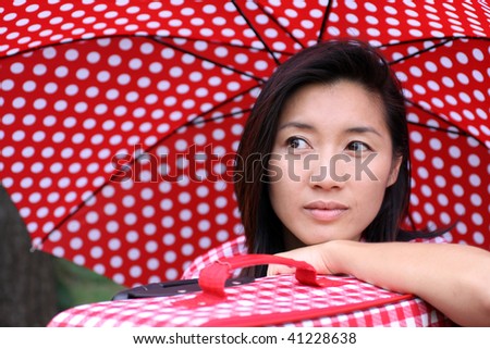 Beautiful Chinese girl leaning on her suitcase with dotted umbrella