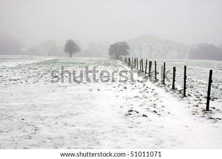 Foggy snow-covered field with wooden fence in Europe