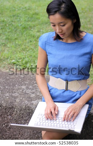 Attractive Chinese woman in dress working outdoors with her laptop