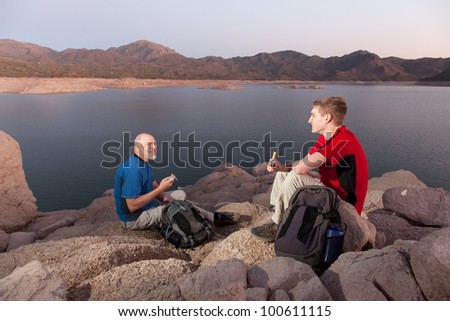 Two Hikers with Backpacks Eating Snacks