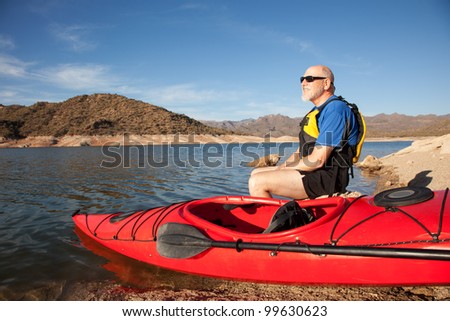 Senior Man Resting on Lakeshore with Kayak. Set against a harsh and rugged desert landscape (Bartlett Lake, Arizona)