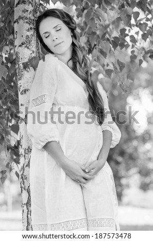 white and black portrait of pregnant woman, ukrainian style, white dress, in the trees, park