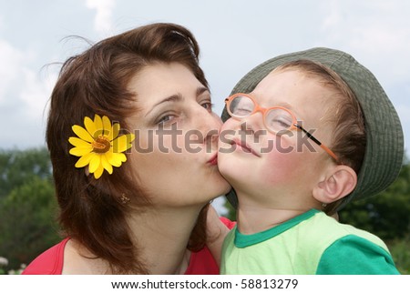 Young beautiful mother kissing her son,background nature