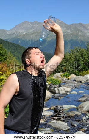 A young man pours water on his head from a plastic bottle, white mountain river, mountain top