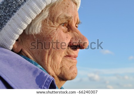 Portrait of an elderly woman, lost in thought, watching the distance, blue sky background