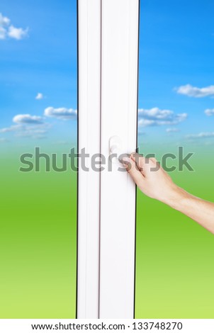 Hand opens window with green field and blue sky as nature background