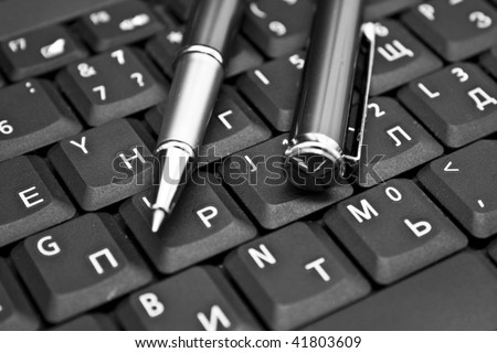 Ballpoint pen resting on computer keyboard. Blue tone, focus on pen tip.