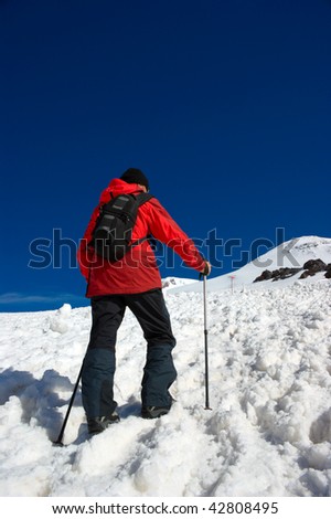 Rock-climber in a red jacket and with rises ski poles on the top of mountain