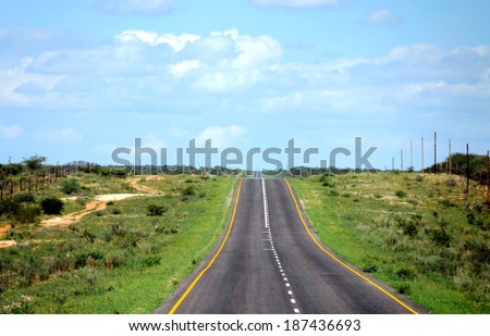 A paved road with green grass on the sides and blue sky above