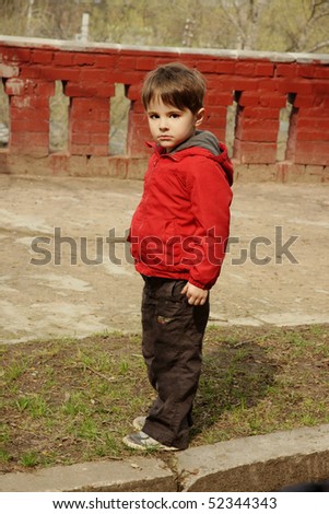 Beautiful little boy in red jacket with serious look, outdoor shot