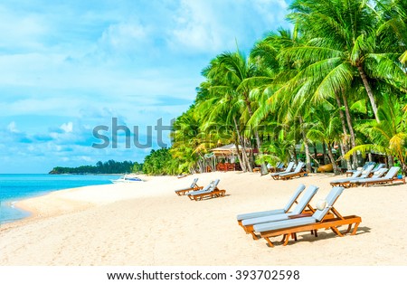 Beach chairs on the white sand beach with cloudy blue sky and sun. Vacation concept