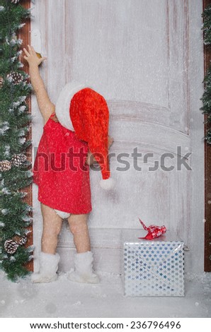 Girl dressed as Santa with gift opens door under snow