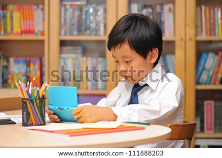 Asian schoolboy in white shirt distracted by portable game machine during homework time