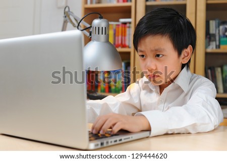 Frustrated Asian school boy in white shirt looking at laptop computer