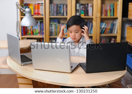 Frustrated young Chinese school child in front of multiple laptop computers