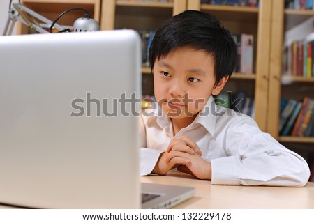 Happy Asian school boy in white shirt in front of laptop computer