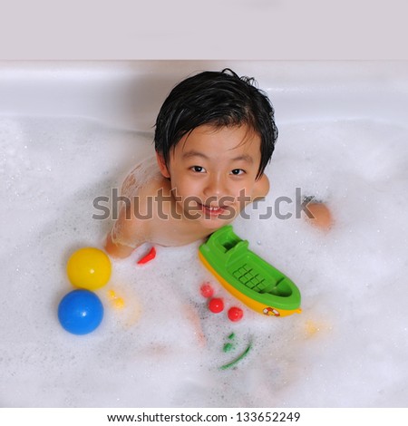 Smiling Asian boy having bubble bath with toys