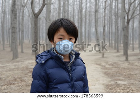 Asian boy wearing mouth mask standing in front of dry forest affected by pollution