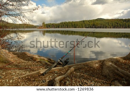 Fishing rod placed on the ground near a  lake outdoors at a recreational area .