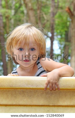 A toddler climbs up and looks over a wall at the park.