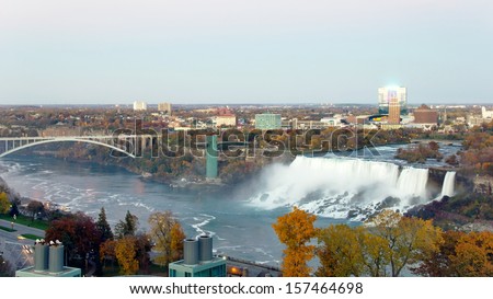 View of Niagara Falls, New York from Niagara Falls, Canada of the American Falls, Rainbow Bridge and the Niagara River as dusk settles in on a late autumn evening in wide screen, 16.x9 resolution.