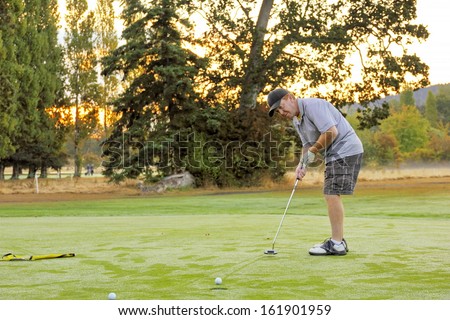The golf ball runs slowly across the green to the cup leaving trails in the heavy dew on the autumn morning golf green as the sun rises behind the golfer's shoulder promising dryer greens soon.