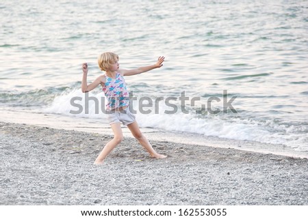 A young blonde girl throwing a rock to skip rocks at Centennial Beach on Lake Ontario in Hamilton, Ontario, Canada, at dusk.