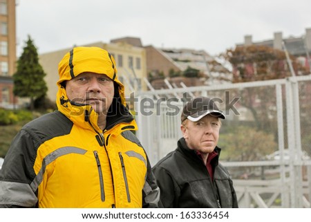 Two mature men out walking in an urban area on a dismal raining day in Victoria, British Columbia, with a wistful glance as they pass by the camera.