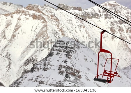 An empty ski lift chair bringing color amid the otherwise colorless world of a mountain ski hill.