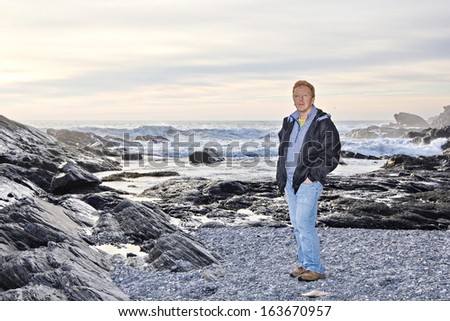 A middle-age male stands on a rocky beach in the winter at Botanical Beach, Port Renfrew, BC, Canada as the sun is low in the sky and the high tide is nearing.