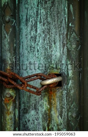 An old rusted chain and lock on old ornate metal door with green patina.   (Focus on chain and eye bolt)